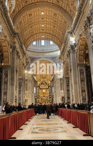 Turisti e pellegrini che camminano attraverso la navata centrale della Basilica di San Pietro con barricate rosse pavimento in marmo soffitto dorato e maestosi interni della chiesa nella città del Vaticano. Foto di alta qualità Foto Stock