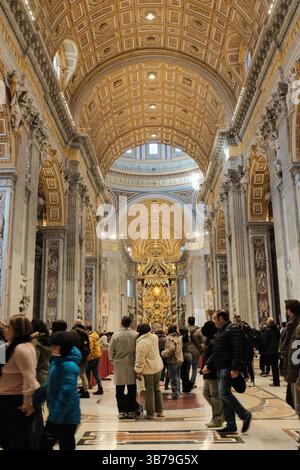 Turisti e pellegrini che camminano attraverso la navata centrale della Basilica di San Pietro con barricate rosse pavimento in marmo soffitto dorato e maestosi interni della chiesa nella città del Vaticano. Foto di alta qualità Foto Stock