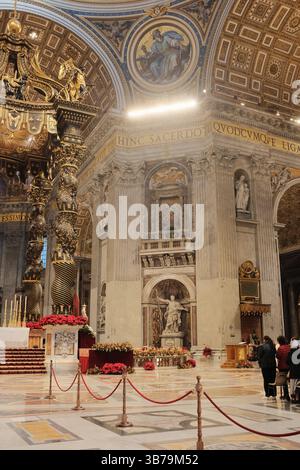 Baldacchino ornato sull'altare papale nella Basilica di San Pietro città del Vaticano progettato da Gian Lorenzo Bernini con colonne in bronzo ritorto decorazioni floreali rosse e iscrizioni latine sotto la grande cupola. Foto di alta qualità Foto Stock