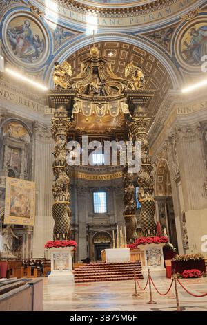 Baldacchino ornato sull'altare papale nella Basilica di San Pietro città del Vaticano progettato da Gian Lorenzo Bernini con colonne in bronzo ritorto decorazioni floreali rosse e iscrizioni latine sotto la grande cupola. Foto di alta qualità Foto Stock