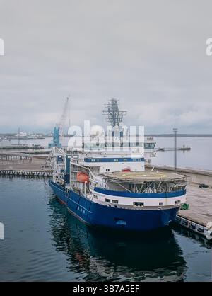 Una nave ormeggiata in un porto, in manutenzione. Nave blu e bianca al molo contro un pesante cielo nuvoloso. Vista frontale Foto Stock