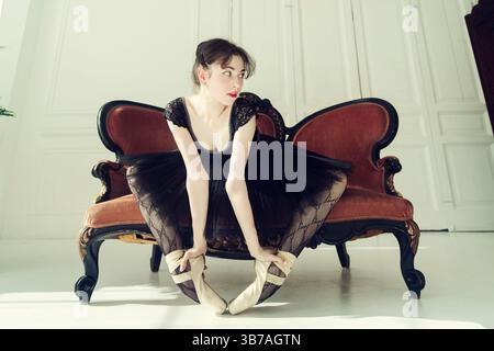Una giovane ballerina con collant in laccetto e pizzo posa seduta su un divano, ritratto di una ballerina Foto Stock