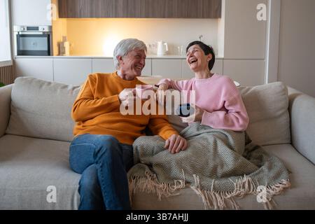 Ridendo, felice, rilassato, una coppia matura che si diverte sul divano mentre parla e si condivide durante i fine settimana Foto Stock
