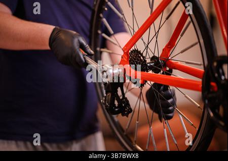 Primo piano delle mani con i guanti utilizzando una chiave a cricchetto per fissare la ruota posteriore di una moto rossa, concentrandosi sul complessivo trasmissione. Foto Stock