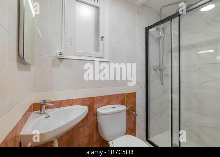 Bagno compatto con piastrelle bianche e arancioni, lavandino ad angolo, WC e doccia in vetro Foto Stock