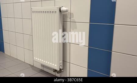 Moderno radiatore bianco su pareti piastrellate con motivo a scacchi blu e bianco in un ambiente interno contemporaneo per esigenze di riscaldamento efficienti. Foto Stock