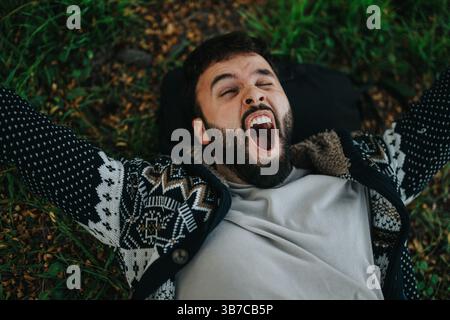 Uomo che si rilassa all'aperto mentre sdraiato su una coperta e sbadiglia ampiamente Foto Stock