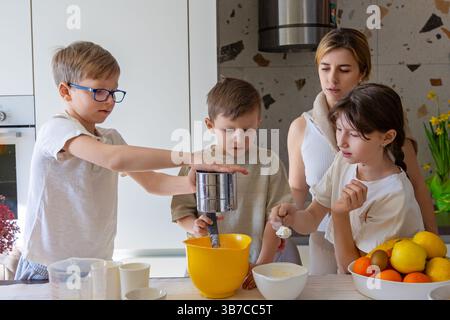 I bambini cuociono con la madre in cucina, la famiglia si lega alla cucina. Foto Stock
