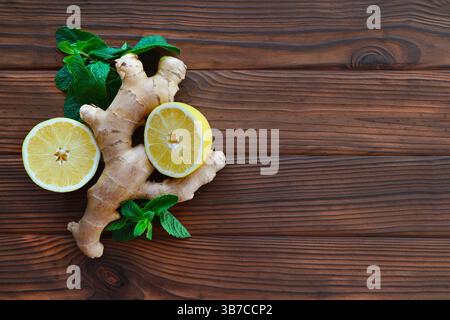 Radice di zenzero, metà di limone e foglie di menta sulla superficie di legno. Una nuova disposizione di radice di zenzero, due metà di limone e foglie di menta vibranti Foto Stock