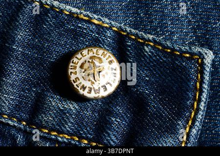 Primo piano del bottone dei jeans ZU Elements che mostra dettagli in metallo con il marchio, mettendo in risalto la maestria e l'identità dell'etichetta italiana in denim Foto Stock