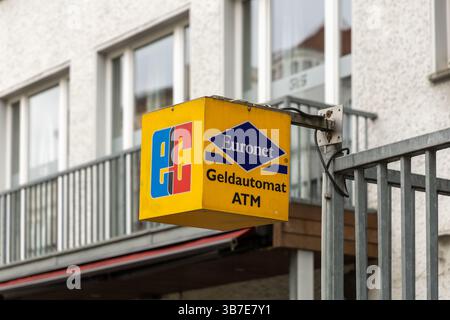 Primo piano di un cartello giallo Euronet ATM con il logo EC su una strada in Germania, montato su un palo metallico contro un edificio residenziale sullo sfondo. B Foto Stock
