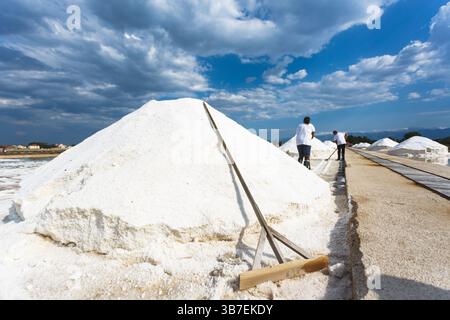 Raccolta tradizionale del sale nelle saline costiere. I lavoratori raccolgono manualmente il sale marino formato dall'evaporazione solare, creando un impressionante sale bianco. Foto Stock