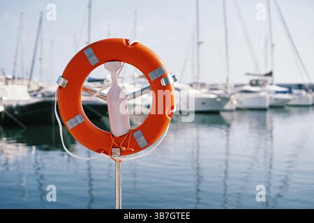 Salvagente rosso su un supporto in metallo con chiusura in plastica bianca sul mare. Foto Stock
