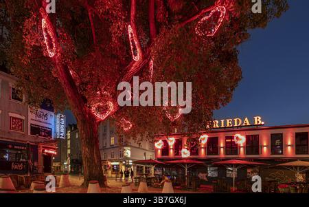 Un albero con luci rosse a forma di cuore decora una vivace scena urbana di notte, Hans-Albers-Platz, St. Pauli, città libera e anseatica di Amburgo, Germania Foto Stock