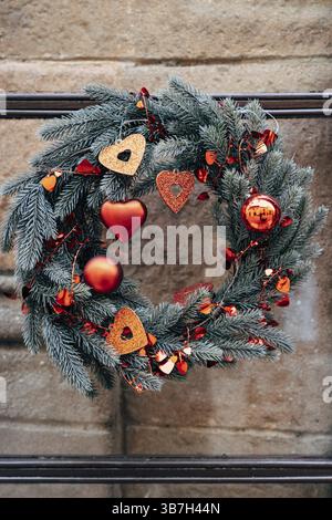 Corona di Natale di rami di abete con decorazioni natalizie rosse su un muro di pietra. Foto Stock