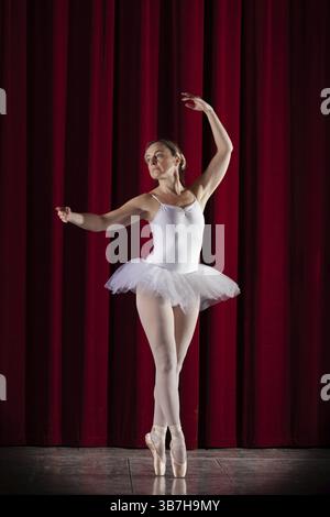 Ballerina di balletto in tutu di danza bianca davanti a una tenda rossa in posa elegante, Mindelheim City Theatre, Mindelheim, Baviera, Germania, Europa Foto Stock