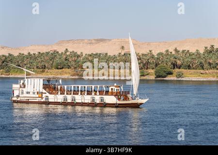 Nave da crociera sul Nilo Dahabiya navigando lungo un deserto sabbioso con palme sul fiume Nilo vicino ad Assuan Foto Stock