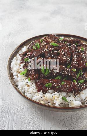 Manzo croccante, con cipolle verdi e semi di sesamo, su una risaia, in una ciotola con bacchette, su una superficie ruvida, nessuno Foto Stock