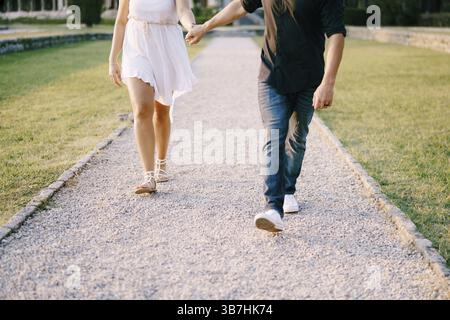 Uomo e donna che camminano lungo il sentiero di ghiaia nel parco tenendosi per mano. Foto Stock