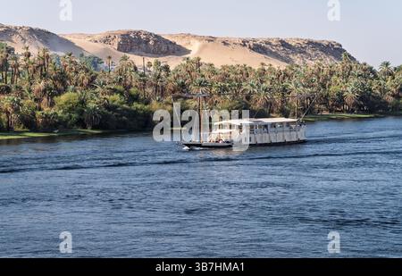 Nave da crociera sul Nilo Dahabiya navigando lungo un deserto sabbioso con palme sul fiume Nilo vicino ad Assuan Foto Stock