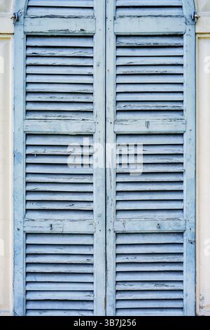 Vecchie persiane blu sulla parete luminosa della casa. Foto Stock