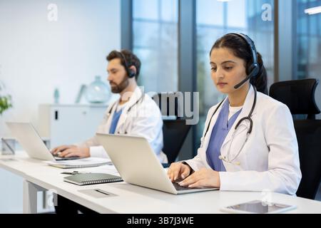 Due medici si trovano in un ufficio, indossando cuffie e utilizzando computer portatili. Essi possono fornire consulenze mediche a distanza. Foto Stock