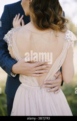 Le mani dello sposo abbracciano la sposa nella parte inferiore della schiena. Vista posteriore. Primo piano. Foto Stock