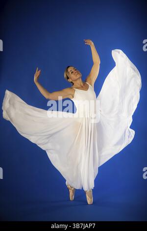 Una ballerina di balletto con un abito bianco che scorre posa graziosamente di fronte a uno sfondo blu, tiro in studio, Mindelheim, Unterallgaeu, Baviera, Germania Foto Stock