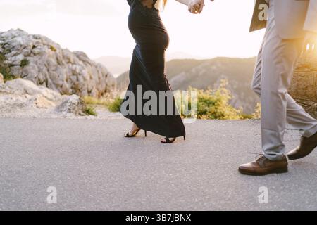 L'uomo e una donna incinta camminano lungo una strada asfaltata in montagna. Primo piano. Foto Stock