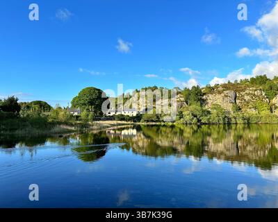 Cottage in pietra che si affacciano sul lago Llyn Padarn a Snowdonia, Galles, circondati da ardesia, alberi e lontane vedute delle montagne. Foto Stock