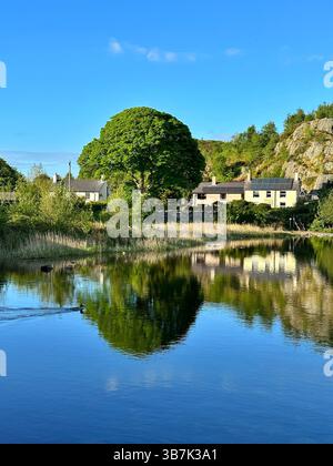 Cottage in pietra che si affacciano sul lago Llyn Padarn a Snowdonia, Galles, circondati da ardesia, alberi e lontane vedute delle montagne. Foto Stock