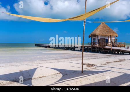 Molo in legno con capanna di palapa che si estende su acque turchesi poco profonde a Holbox, Messico. Foto Stock