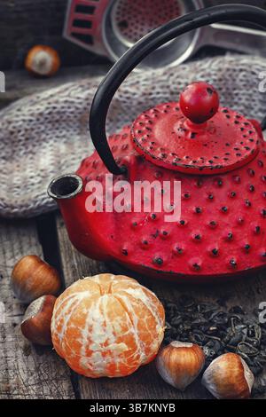 Bollitore in ghisa rosso, mandarino, foglie di tè su fondo in legno Foto Stock