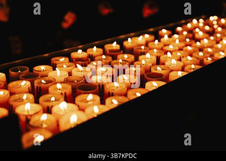 Le candele votive bruciano su uno stand in una chiesa al buio. Foto Stock