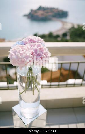 Il bouquet di ortensie rosa si staglia in un alto vetro trasparente su un piedistallo. Foto Stock