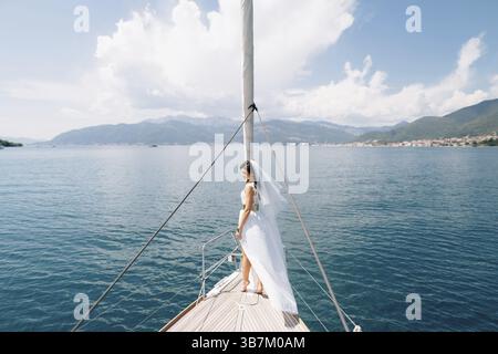 La sposa si erge sulla prua dello yacht che naviga nella baia di Cattaro, vista sul retro. Foto Stock