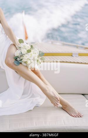 La sposa con un bouquet siede a bordo di uno yacht che naviga sul mare. Ritagliato. Senza volto. Foto Stock