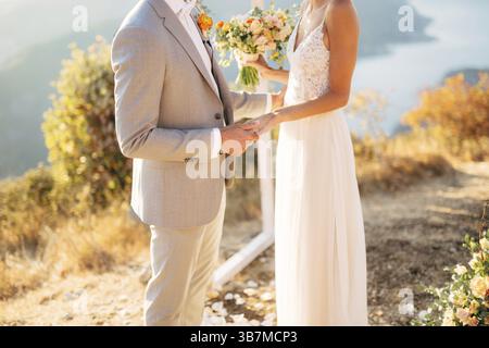 La sposa e lo sposo sono in piedi sul Monte Lovcen vicino all'arco nuziale e si tengono per mano. Foto Stock
