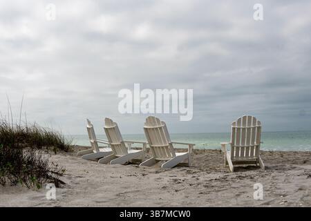 Florida, 4 sedie bianche in lastre di adorandack su una spiaggia. da dietro. Acqua davanti. Foto Stock