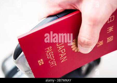 Primo piano della mano di un giovane con un passaporto e una carta d'imbarco nel mezzo, che sta per partire per un viaggio con una valigia Foto Stock