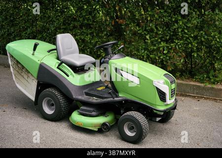 Il grande rasaerba verde si trova sull'asfalto vicino alle boccole. Foto Stock