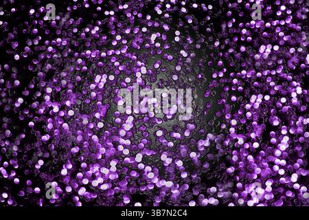 Luci bokeh astratte di colore viola e bianco che ruotano su uno sfondo scuro, perfette per le feste.Bielorussia Foto Stock