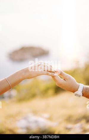 L'uomo tiene per mano una donna con una fede nuziale su una montagna sopra il mare. Ritagliato. Senza volto. Foto Stock
