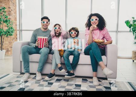 Famiglia felice che guarda i film insieme sul divano nell'accogliente soggiorno con occhiali 3D e gusta spuntini in una giornata di sole nel fine settimana. Foto Stock