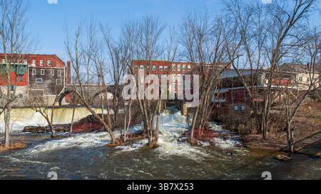 Cascate di Middlebury sull'Otter Creek con edifici storici e un ponte in pietra sopra, alte acque sorgive a Middlebury, Vermont, Stati Uniti. Foto Stock
