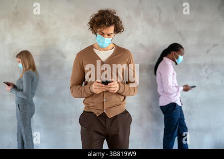 Persone in stile business e maschere mediche in piedi con gadget e mantenere la distanza sociale. Foto Stock