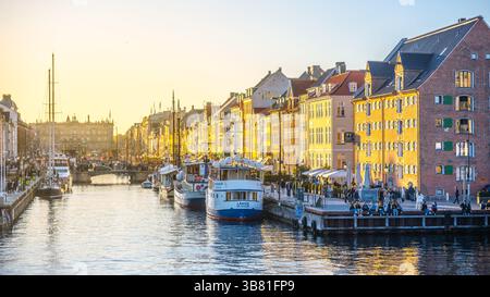 Nyhavn a Copenhagen mostra uno splendido tramonto, proiettando un caldo bagliore sugli edifici colorati e sul vivace lungomare. La gente gode dell'atmosfera vivace lungo il canale. Foto Stock