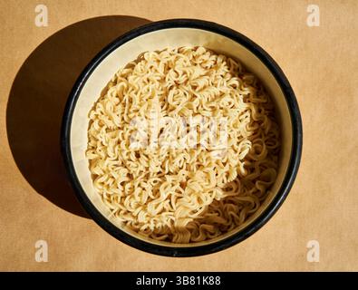 Spaghetti istantanei cotti serviti su un piatto di ceramica su fondo marrone. Concetto di cibo semplice Foto Stock