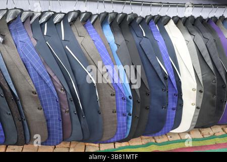 Questa immagine mostra una vivace collezione di giacche appese uniformemente su un rack in metallo. Le giacche variano per motivo, colore e stile, fornendo Foto Stock