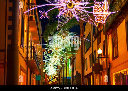Festosa scena di strada, adornata da vivaci luci natalizie a Funchal Madeira. La calda illuminazione si riflette sulle facciate, creando una vacanza magica Foto Stock